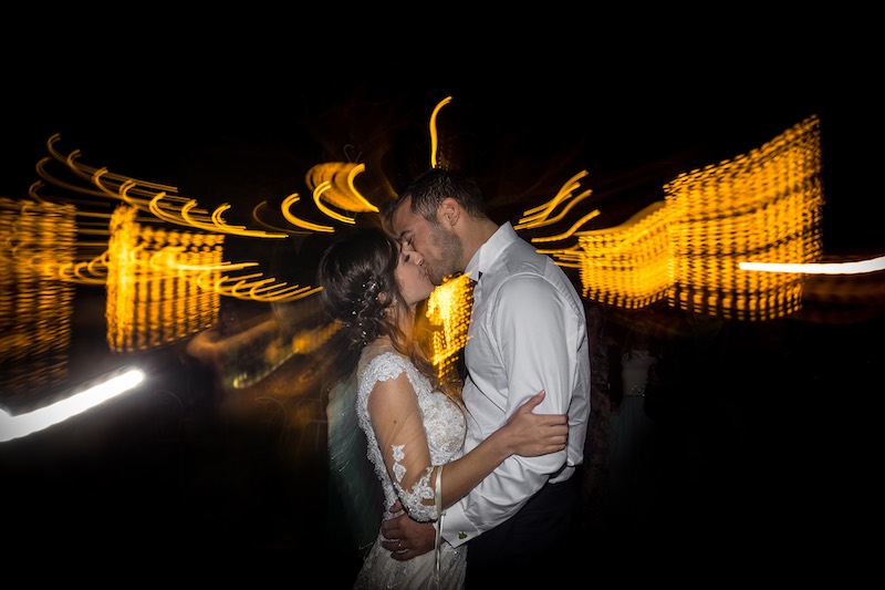 In questa foto di Nicola Tanzella due sposi che si baciano davanti a luci di colore giallo sfocate