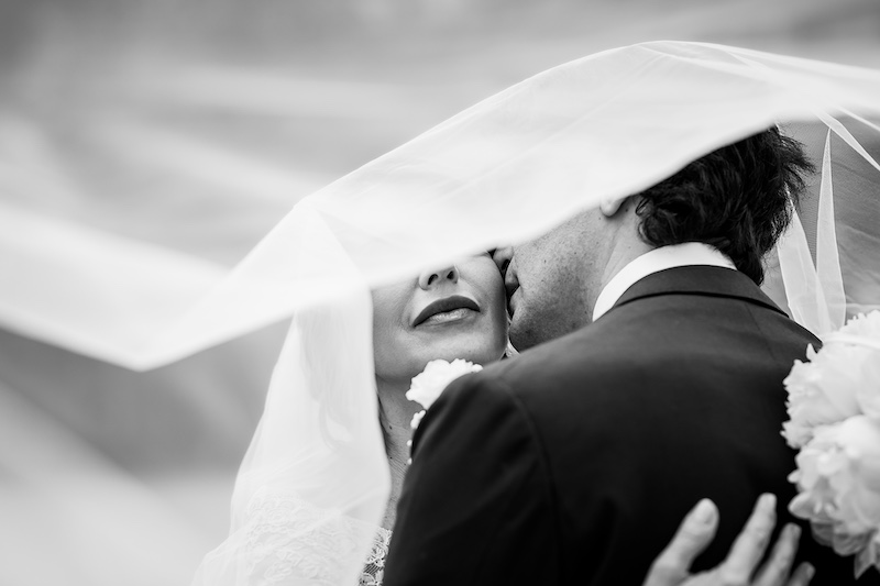 In questa foto di Nicola Tanzella in bianco nero le bocche di due sposi che si abbracciano sotto al velo della sposa