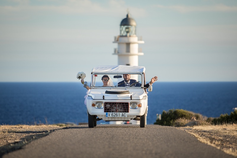 In questa foto di Nicola Tanzella due sposi a bordo di una macchina di colore bianco percorrono una strada con lo sfondo di un faro e del mare