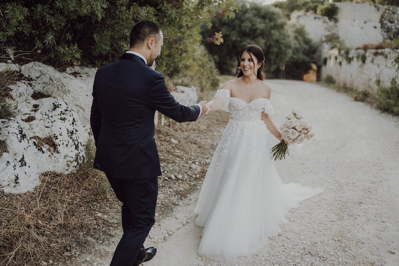 In questa foto dello Studio Santanastasio due sposi camminano su una stradina sterrata prendendosi per mano. Lo sposo è di spalle e tira verso di sé la sposa che gli sorride