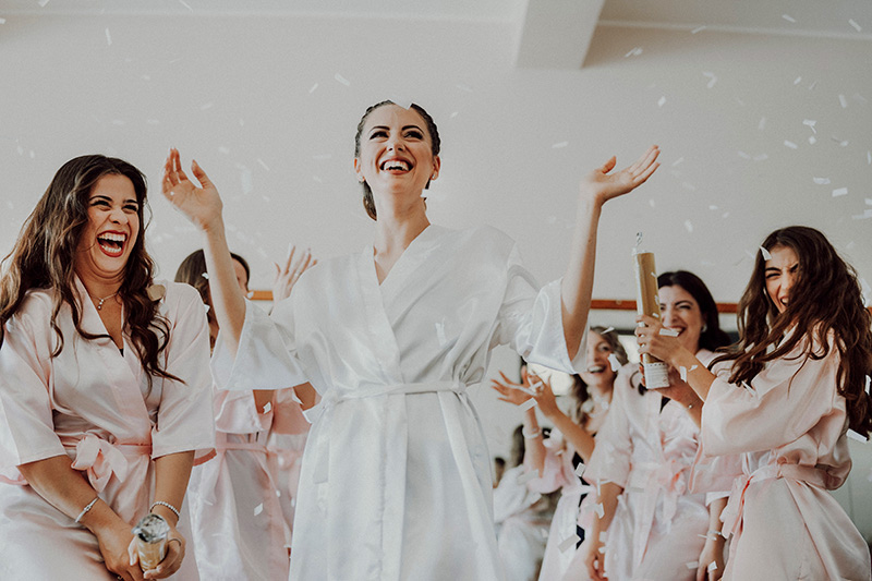 In questa foto dello Studio Santanastasio una sposa festeggia con le sue damigelle durante la sua preparazione. La sposa indossa un kimono di colore bianco; le damigelle indossano lo stesso kimono di colore rosa