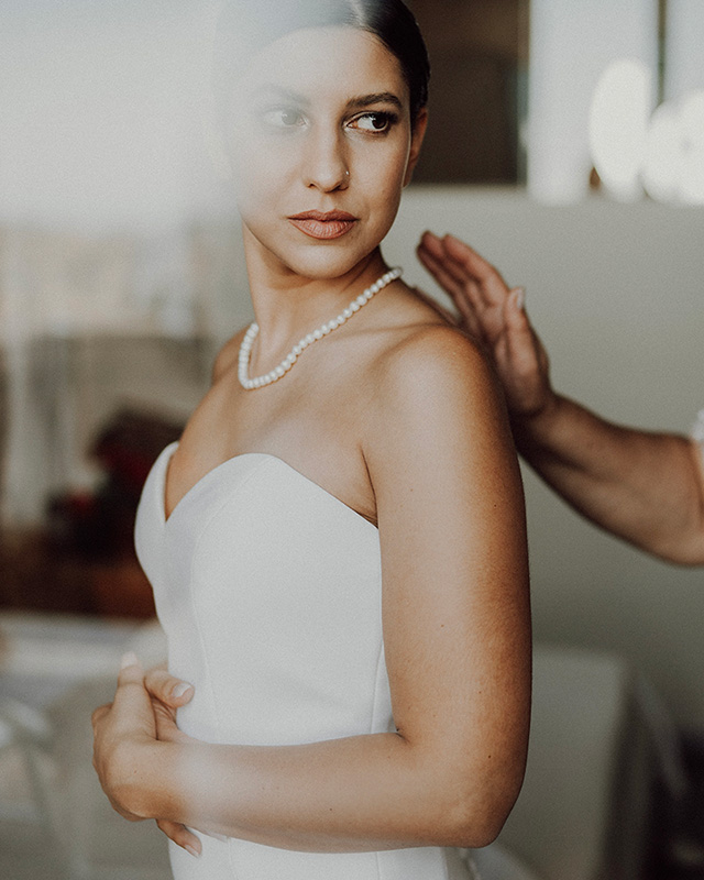 In questa foto dello Studio Santanastasio una sposa inquadrata a mezzo busto durante la preparazione guarda verso sinistra. Indossa un abito da sposa con scollo a cuore e un filo di perle