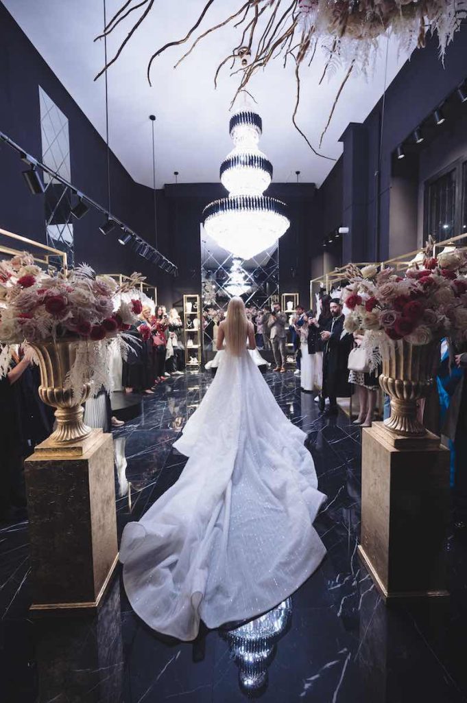 In questa foto una modella di spalle sfila nell'atelier di Milano indossando un abito da sposa con lunghissimo strascico