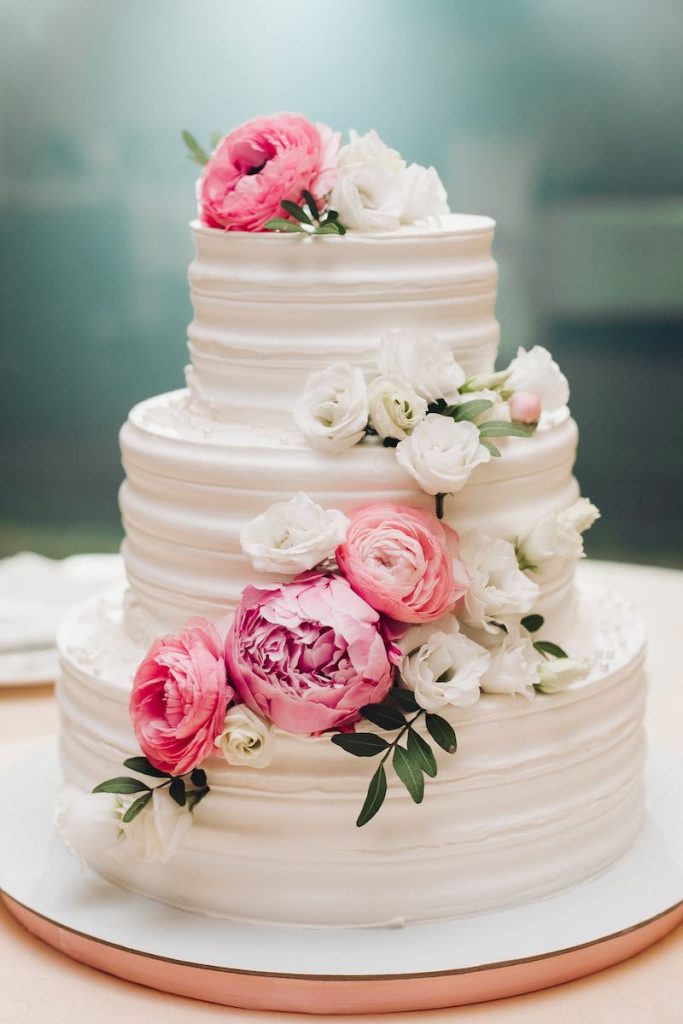 In questa foto una delle torte matrimonio 2023 a 3 piani decorata con glassa bianca e fiori di colore rosa e bianco