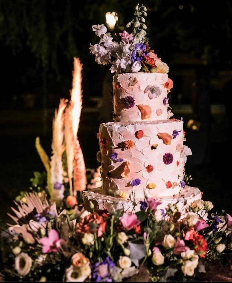 In questa foto una torta per matrimonio decorata con glassa bianca e fiori pressati. Un bouquet di fiori è usato come cake topper