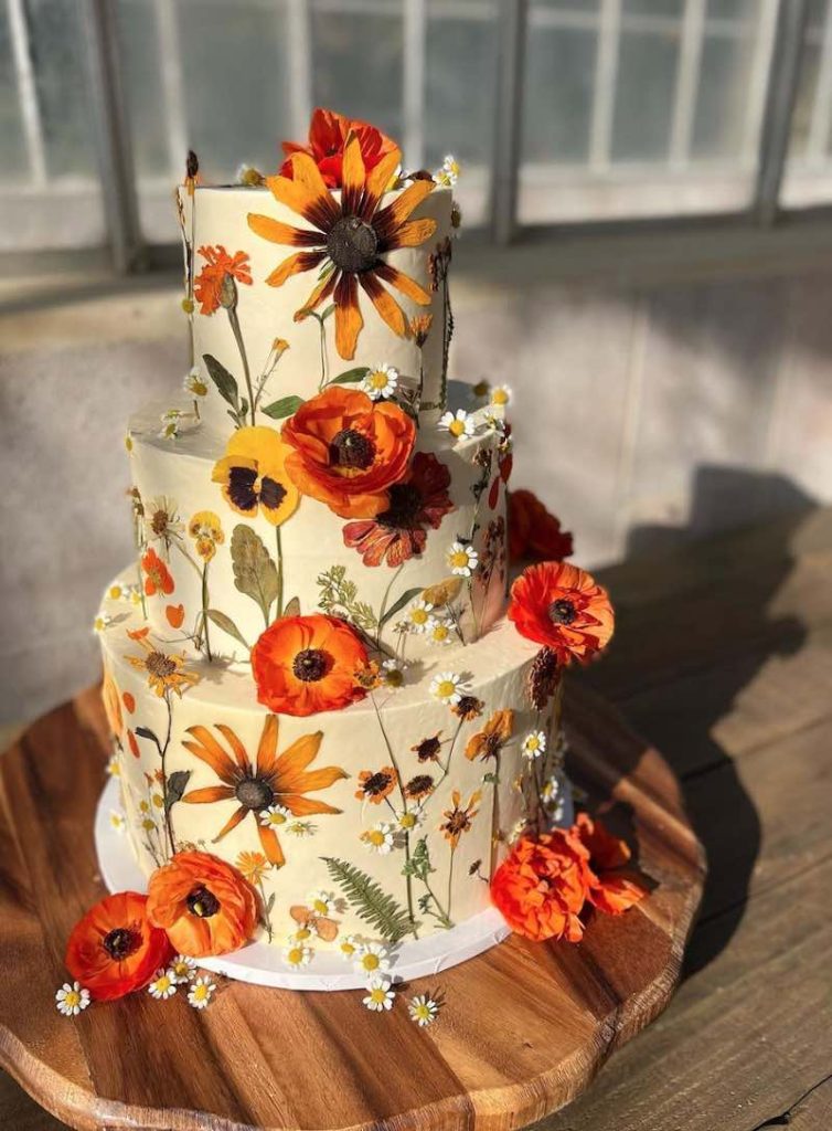 In questa foto una torta per matrimonio a tre piani decorata con glassa bianca e fiori pressati di colore arancione e giallo