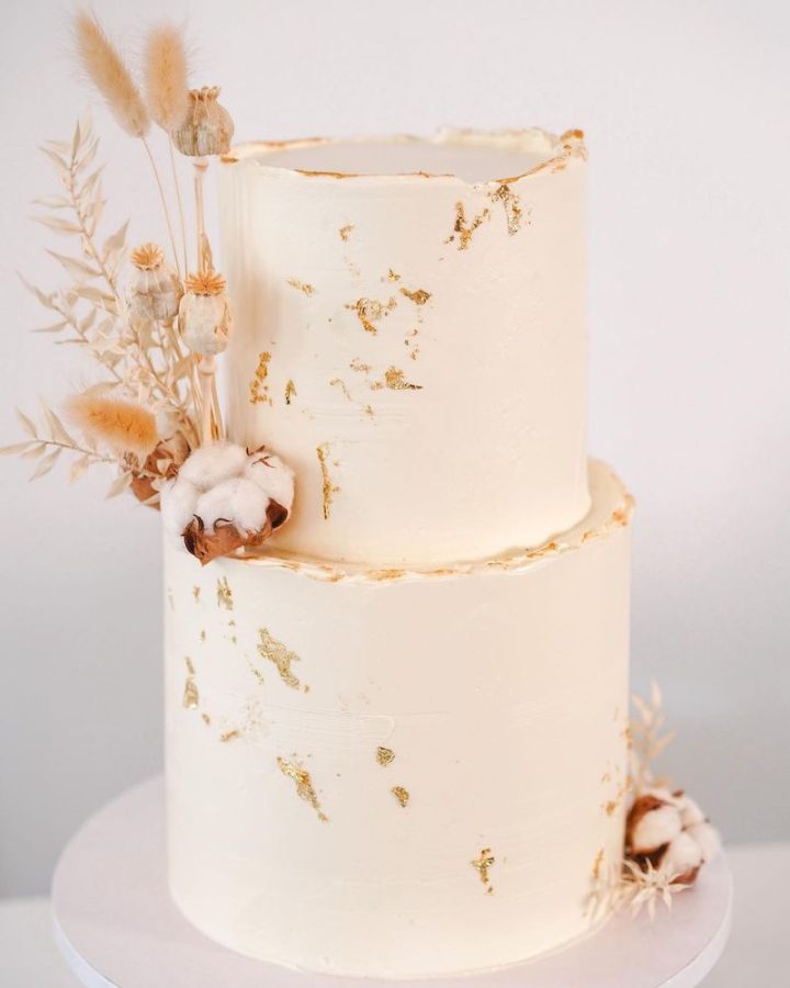 In questa foto una torta per matrimonio a 2 piani decorata con glassa, screziature di colore oro e fiori di cotone 