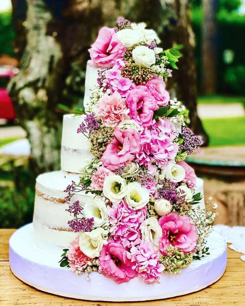 In questa foto una naked cake per matrimonio 2023 a 5 piani decorata con glassa bianca e fiori 