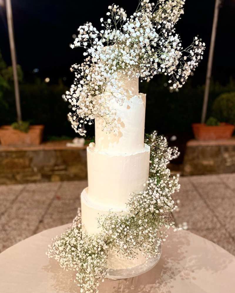 In questa foto una delle torte matrimonio 2023 a 4 piani decorata con glassa di colore bianco e una spirale di gypsophila di colore bianco