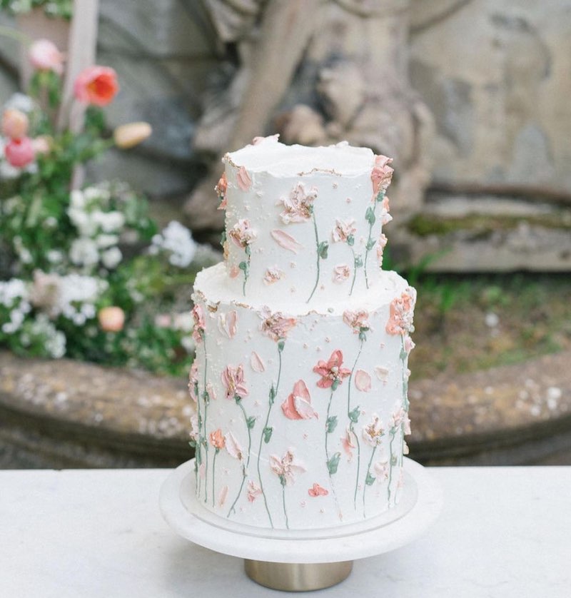 In questa foto una torta matrimonio 20203 decorata con glassa bianca e pennellate di fiori di colore rosa e ramoscelli di colore verde