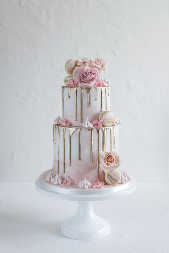 In questa foto una delle torte matrimonio 2023 di tipo drip cake di colore rosa e oro decorata con fiori e macarons