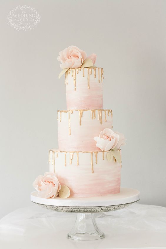 In questa foto una drip cake nei toni del bianco, del rosa e dell'oro decorata con rose di colore rosa