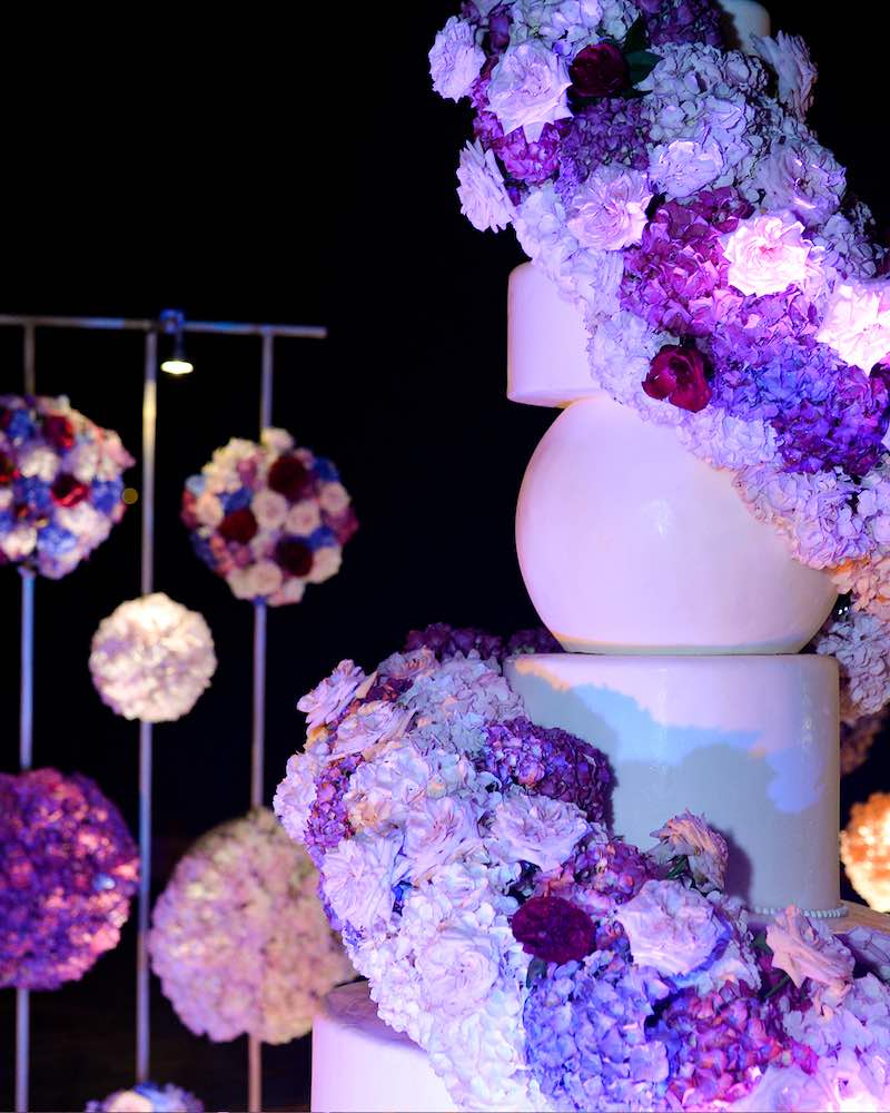 In questa foto una delle torte matrimonio 2023 a piani decorata con glassa di colore bianco e una spirale di fiori di colore lilla e bianco