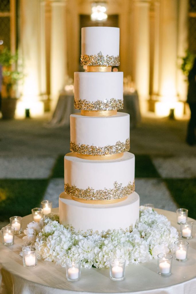 In questa foto una torta nuziale a piani separati di colore bianco e oro decorata con pepite dorate 