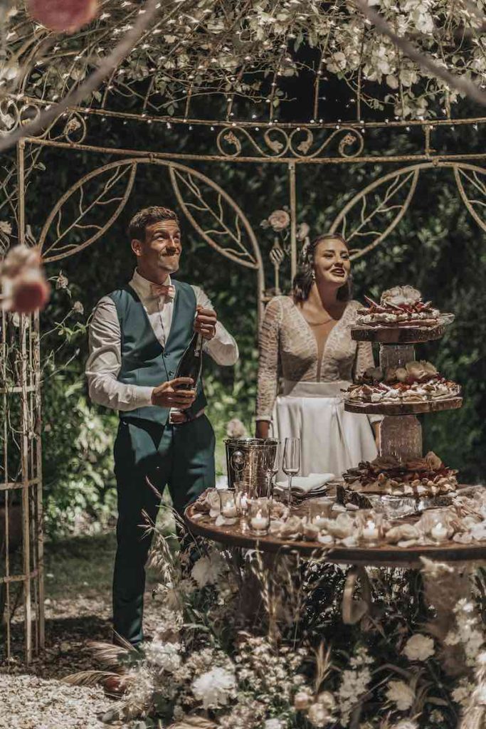 In questa foto due sposi festeggiano davanti ad una torta per matrimonio a piani separati con cilindri di vetro