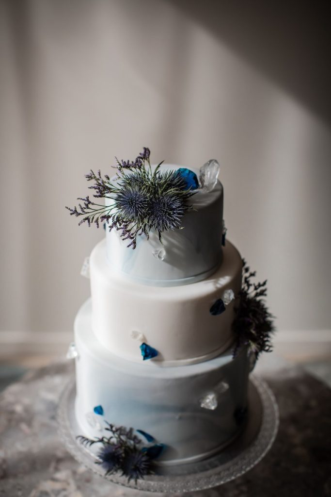 In questa foto una torta nuziale a 3 piani con effetto watercolor di colore azzurro polvere decorata fiori di colore blu