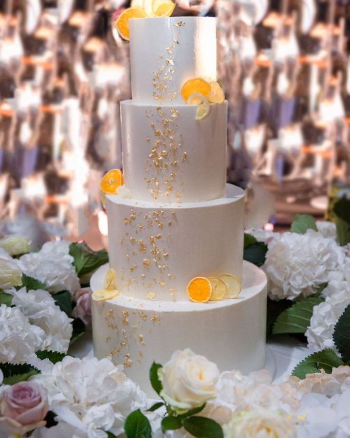 In questa foto una torta per matrimonio a quattro piani decorata con glassa di colore bianco, pepite d'oro e fettine di arancia e limone 