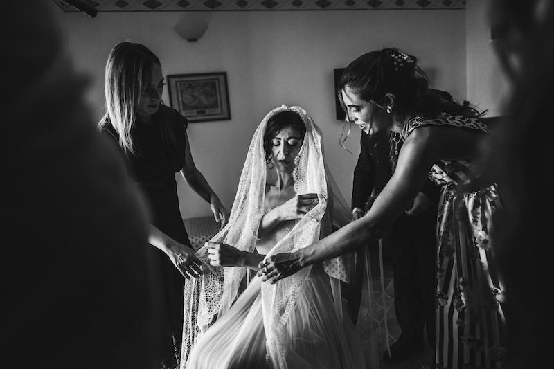 In questa foto in bianco e nero di Vincenzo Aluia una sposa aiutata dalle sue amiche si aggiusta il velo durante la preparazione