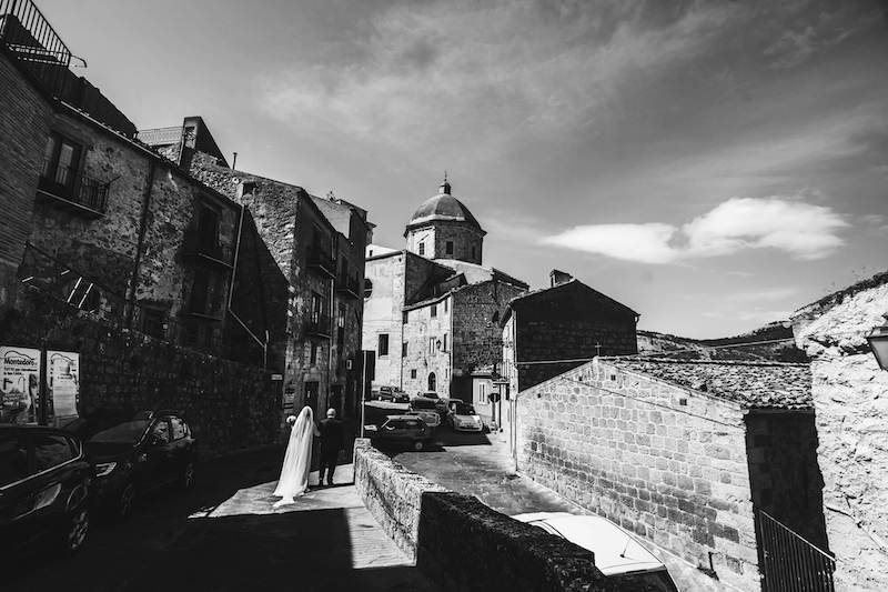 In questa foto in bianco e nero di Vincenzo Aluia una sposa con il suo papà cammina per le strade di Petralia Sottana