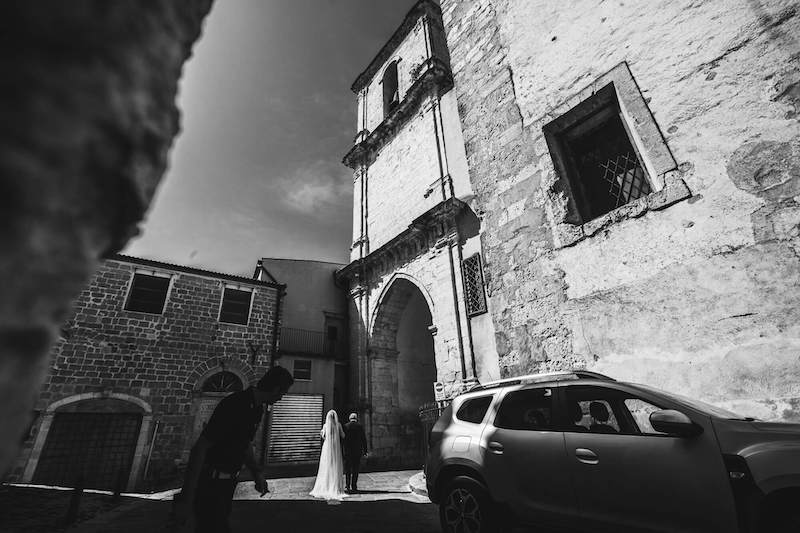 In questa foto in bianco e nero di Vincenzo Aluia una sposa arriva nella chiesa di Petralia Sottana a piedi e al braccio del papà