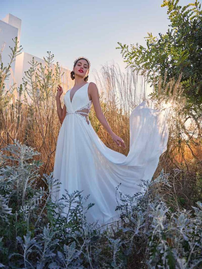 In questa foto una modella indossa un abito da sposa Mysecret sposa 2024 della linea Orchidea modello scivolato in chiffon di seta con dettagli cut out decorati in pizzo sui fianchi 