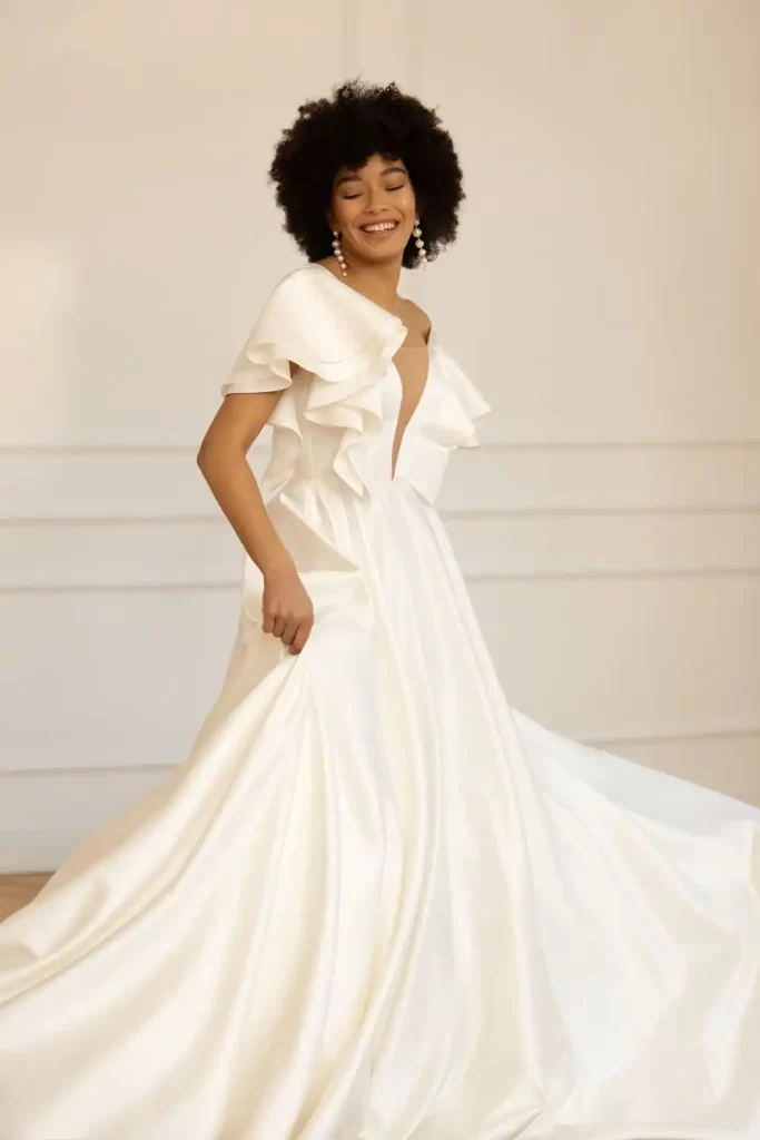 In questa foto una modella indossa un abito da sposa ampio in mikado di seta Eva Lendel 2023 con scollo a V e ruches su petto e maniche 