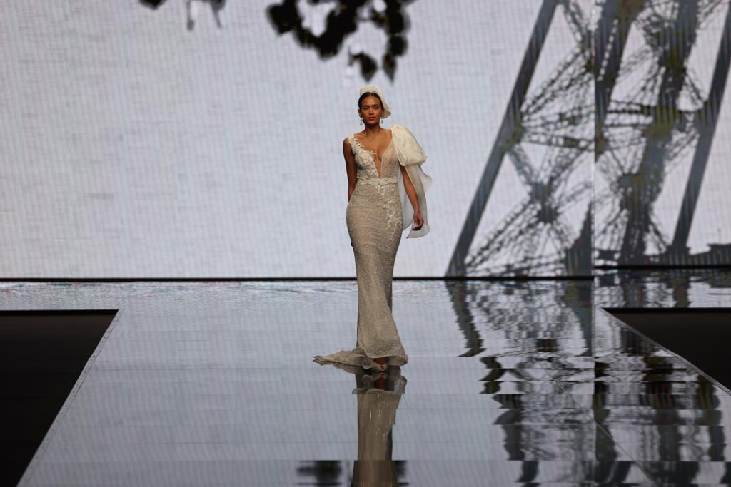 In questa foto una modella sfila indossando un abito da sposa Michela Ferriero 2024 a sirena con ricami floreali e maxi fiocco sulla spalla