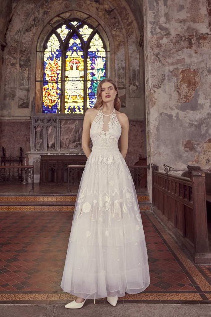 In questa foto una modella indossa un abito da sposa Temperley Bridal 2024 alla caviglia in tulle ricamato e con scollatura all'americana