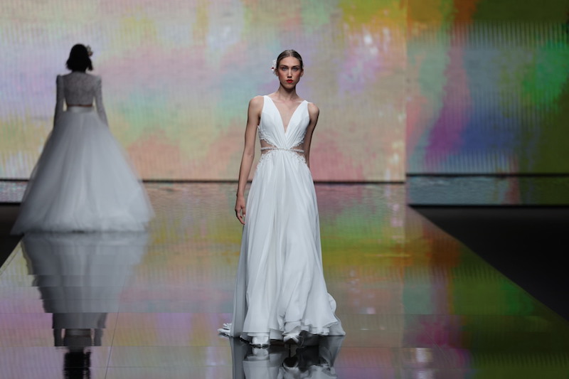 In questa foto una modella sfila indossando un abito da sposa scivolato in chiffon Mysecret Sposa 2024 con scollo a V e dettagli cut-out sui fianchi