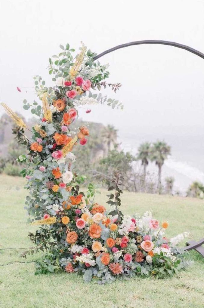 In questa foto uno degli allestimenti matrimoni di Idee da Sogno: un backdrop semicircolare decorato eucalipto e con rose di colore arancione, rosso e bianco