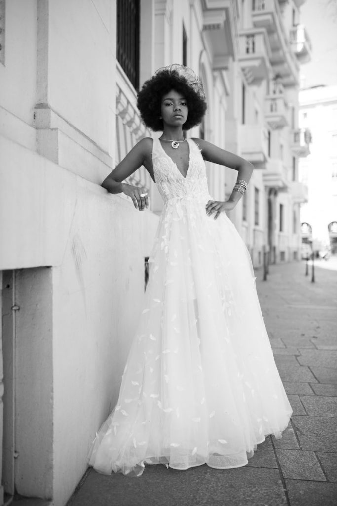 In questa foto in bianco e nero una modella indossa un abito da sposa scivolato con scollo a V e ricami di petali all over della collezione Crystal Le Fate Milano 2024