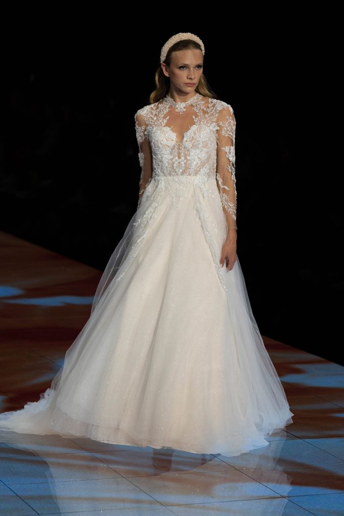 In questa immagine un abito da sposa Modeca 2024 con corpetto in pizzo e un coprispalle in pizzo dall'effetto tattoo. 