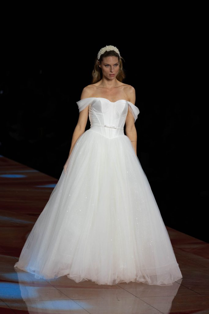 In questa immagine un abito da sposa Modeca 2024 romantico ed elegante, con maniche leggermente cadute e un fiocco in vita.