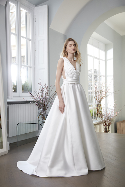 In questa foto una modella posa indossando un abito da sposa bianco ottico, dalla linea strutturata ad A, della collezione Peter Langner Milano 2024