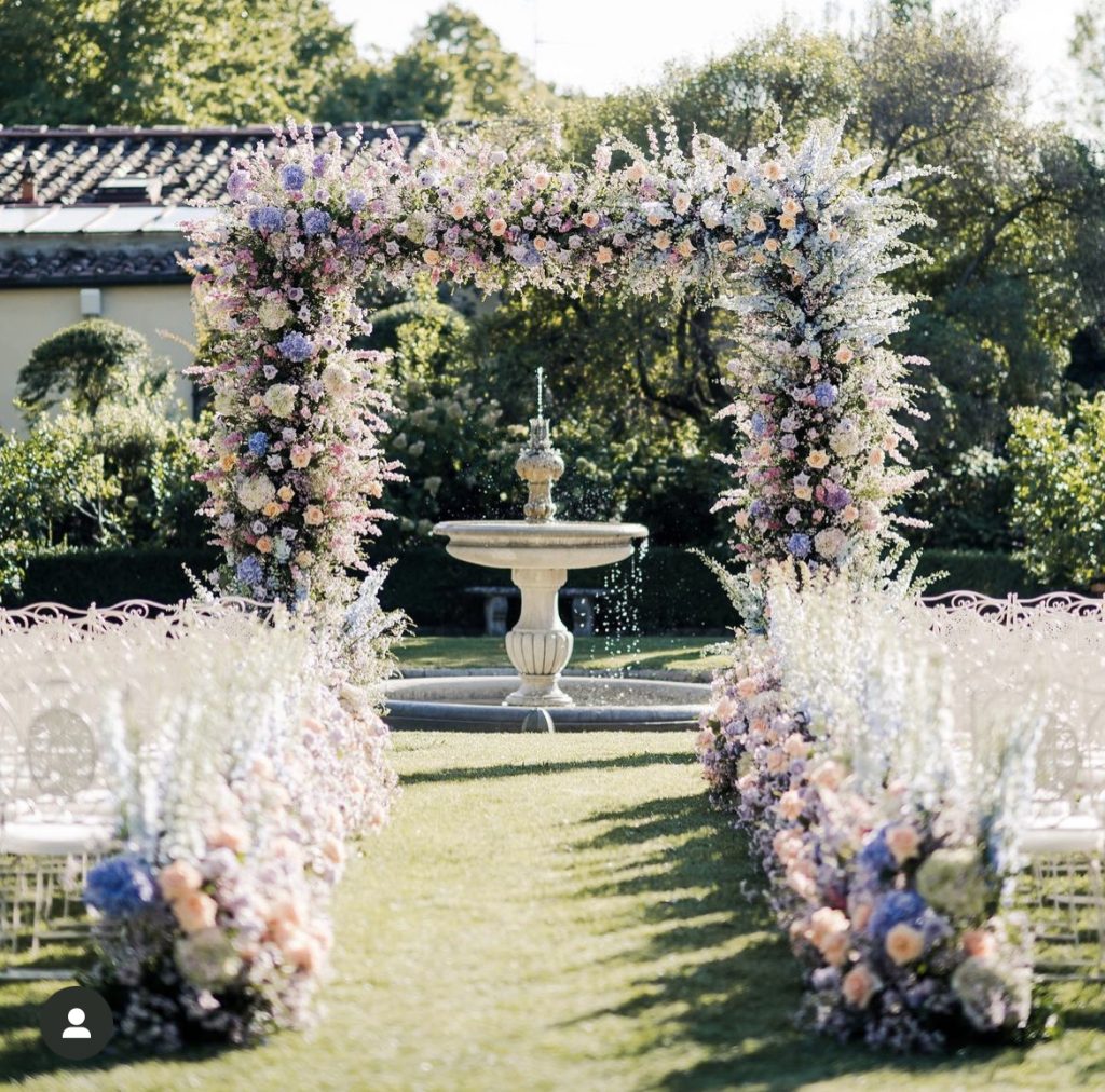 In questa immagine un allestimento per location matrimonio con un arco di fiori e tantissime decorazioni ai lati. 