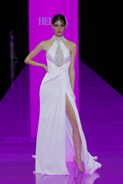 In questa foto una modella sfila sulla passerella della Barcelona Bridal Fashion Week 2023 mentre indossa un abito da sposa con scollatura all'americana di Helena, brand del gruppo Maison Signore