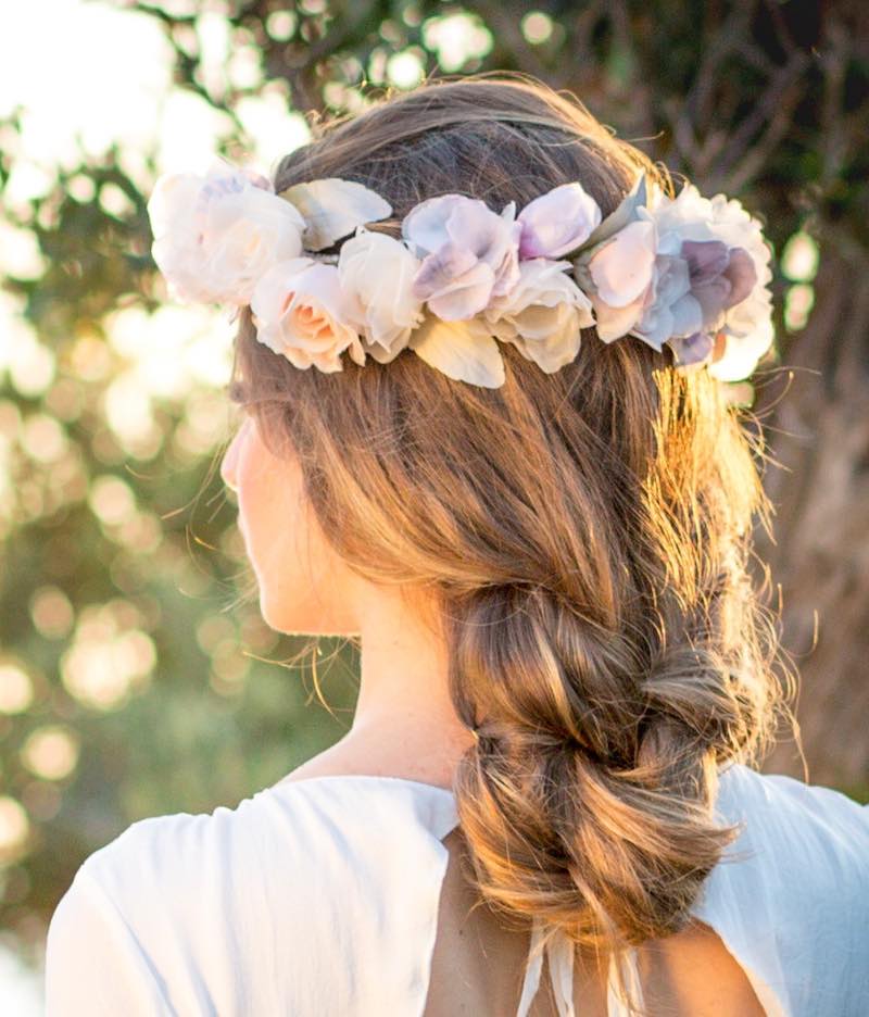 In questa foto una modella ritratta di spalle con una treccia indossa una corona di fiori di seta di Marco Cucinotta nei toni del lilla e del bianco
