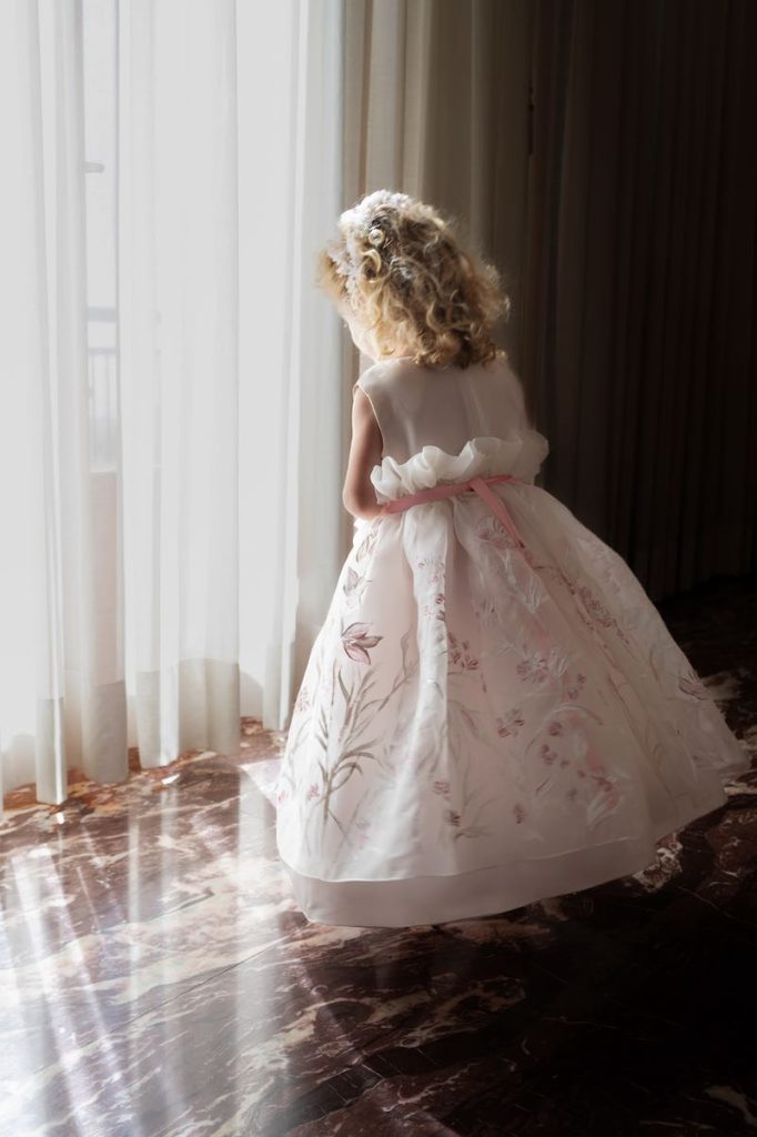 In questa foto una bimba di spalle indossa un abito da damigella con fiori dipinti nei toni del rosa