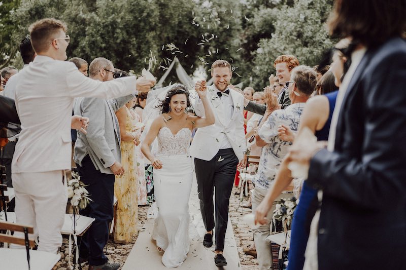 In questa foto due sposi sorridenti corrono sorridendo lungo il corridoio della location del matrimonio civile mentre tutti gli invitati lanciano coriandoli e riso