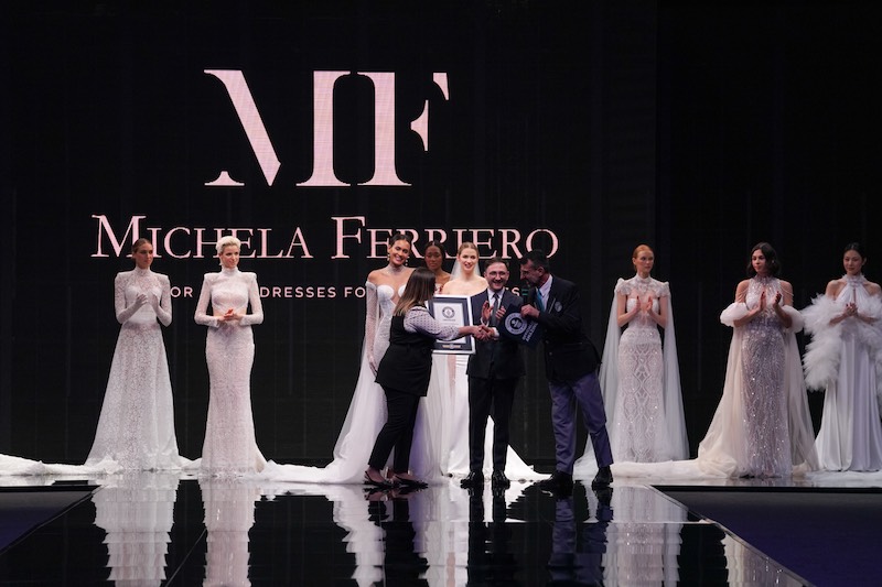 In questa foto la stilista Michela Ferriero riceve l'attestato del Guinness World Record sulla passerella del Sì Sposaitalia con il marito e ceo dell'azienda Lorenzo Albanese circondati da modelle che indossano gli abiti da sposa 2024 della collezione Enchanté