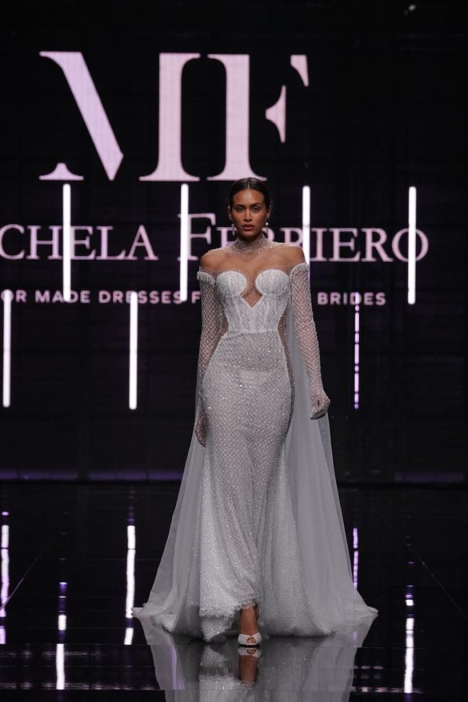 In questa foto una modella sfila con un abito da sposa Michela Ferriero 2024 a sirena con cristalli Swrovski e maniche ampie e leggere per cui la stilista è stata premiata con un Guinness World Record