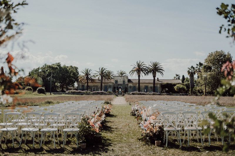 In questa foto una location per matrimonio allestita per un matrimonio civile su un prato con sedie bianche e fiori di colore rosa