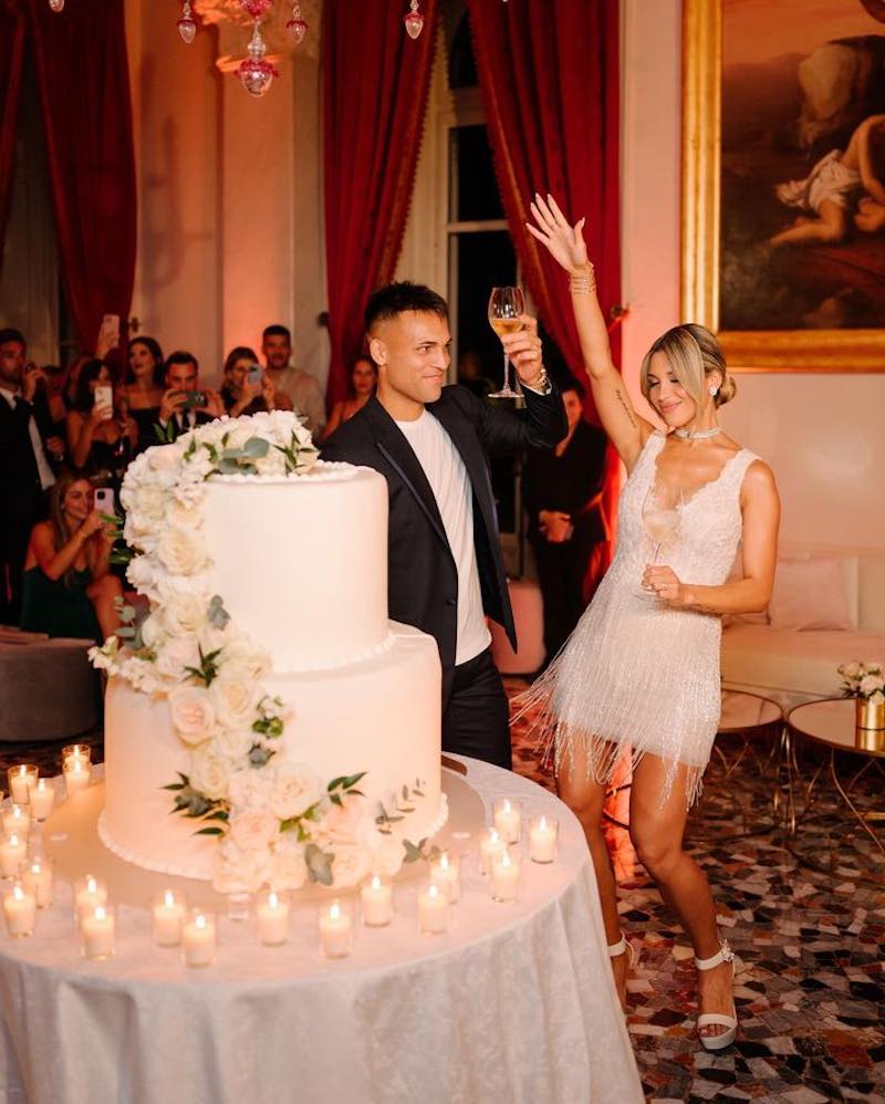 In questa foto Lautaro Martinez e Agustina Gandolfo dietro alla loro torta nuziale a due piani, decorata con fiori di colore bianco e circondata da piccole candele