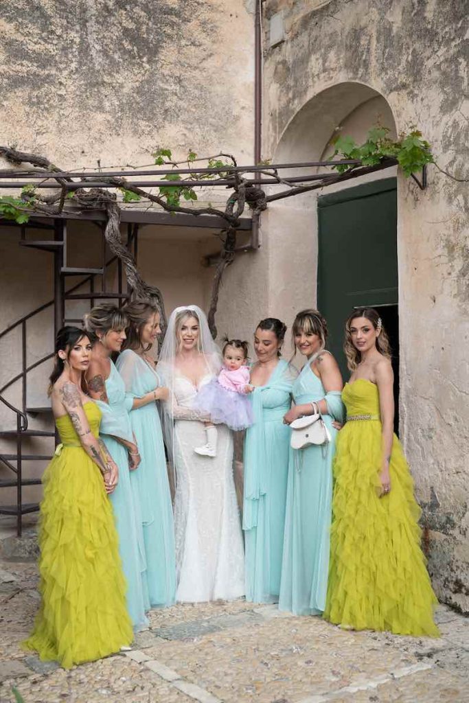 In questa foto Nina Rima in abito da sposa Atelier Emé tiene in braccio la figlia Ella Noa, circondata dalle sue quattro damigelle e le sue due testimoni che indossano un abito da cerimonia color lime con gonna a balze in tulle