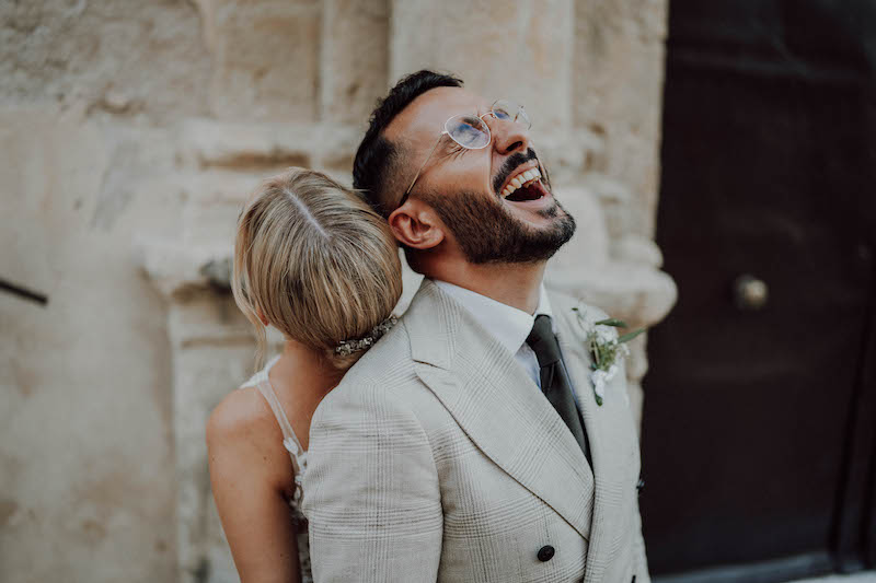 In questa foto uno sposo e una sposa ridono appoggiati l'uno sulla schiena dell'altra 