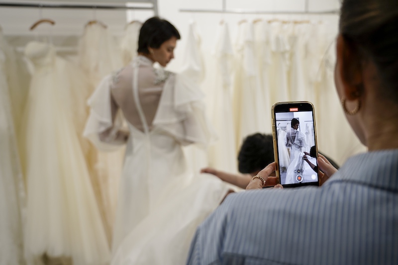 In questa foto una donna di spalle fotografa con lo smartphone una modella in abito da sposa 