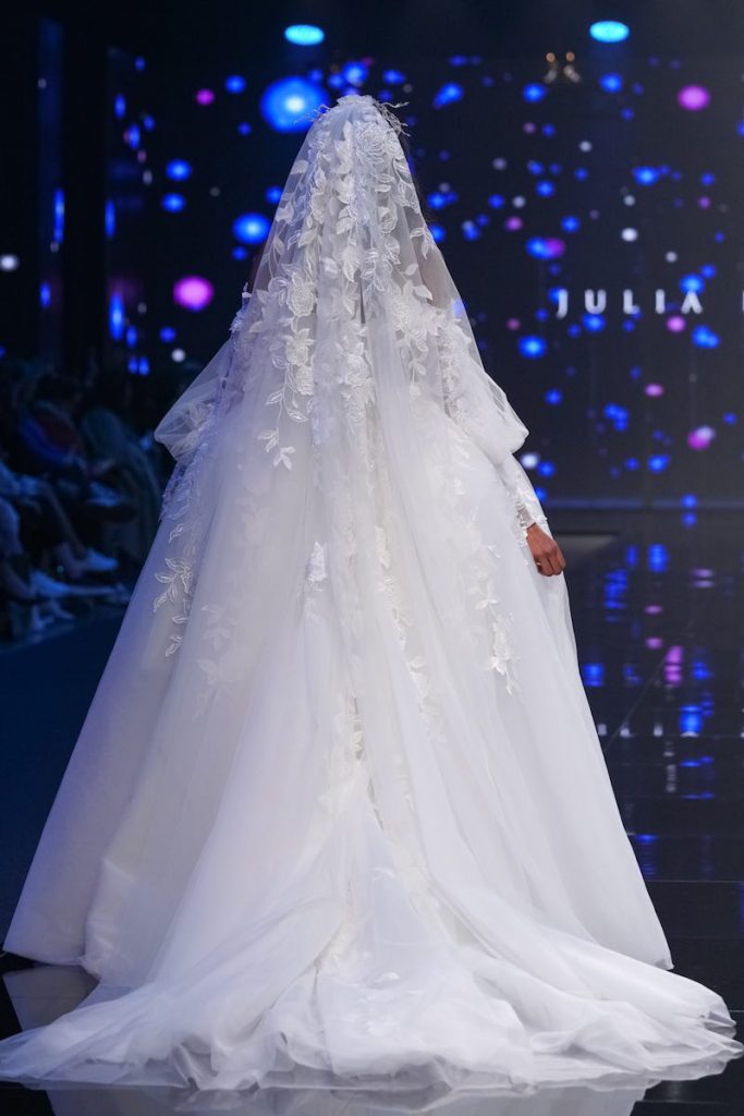 In questa foto una modella sfila di spalle con un velo da sposa con ricami in pizzo di Julia Kontogruni