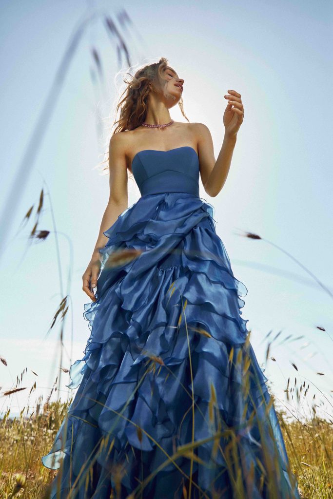 In questa immagine una ragazza indossa un abito della collezione del brand italiano nei toni del blu con la gonna piena di rouches.