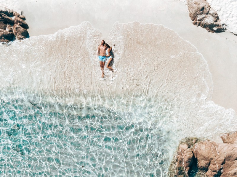 In questa foto una coppia di sposi sdraiati sulla spiaggia della Marinedda durante il viaggio di nozze in un resort Delphina