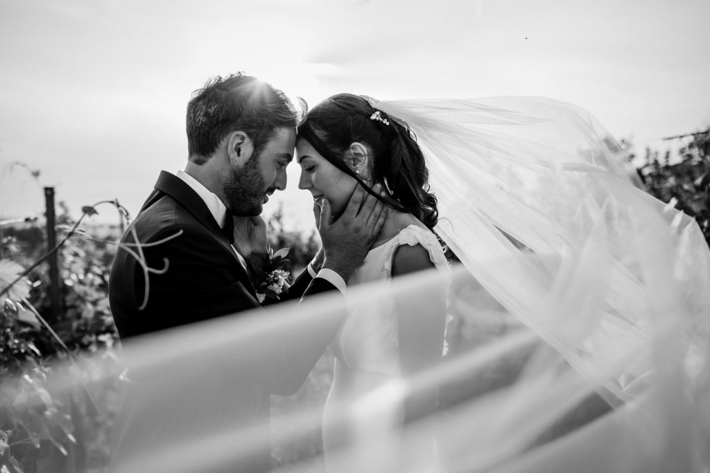 Una foto in bianco e nero del matrimonio di Martina e Federico, realizzato da Edoardo Giorio, tra i fotografi a Torino: i due sposi si scambiano una carezza in campagna avvolti dal velo di lei